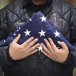Benny Guzman of FDNY Station 20 in the Bronx holds a flag for a fallen EMT after a fatal incident during an evening shift (NYC Mayor's Office)